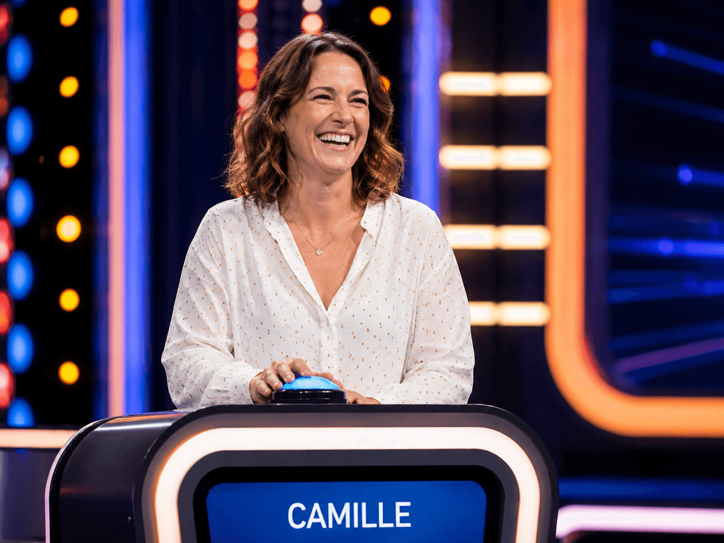 Candidate souriante derrière son pupitre, sur le plateau d'un jeu télévisé